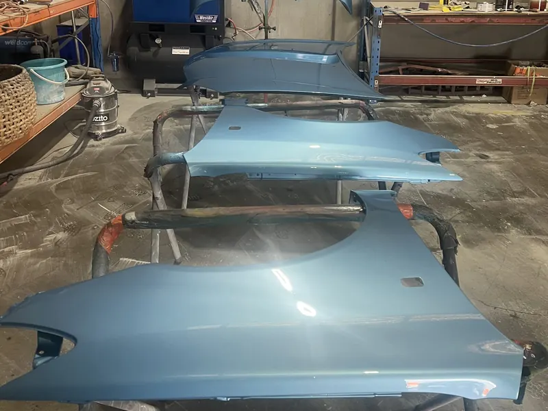 Light blue guards and a bonnet freshly painted on stands in the workshop