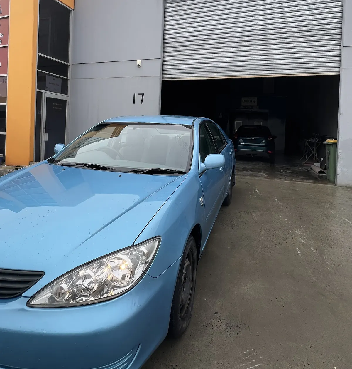 A light blue sedan parked outside the roller door of Factory 17