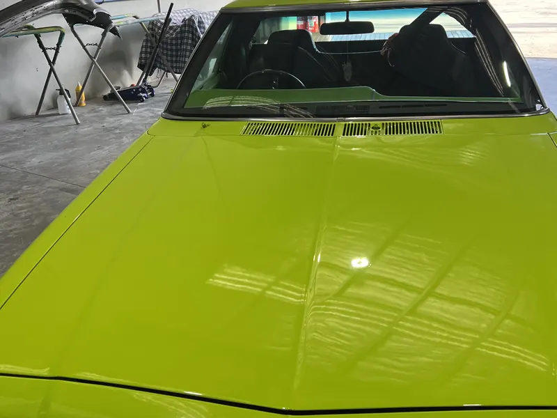 The bonnet of a classic car in glossy bright green paint, looking out of the workshop door