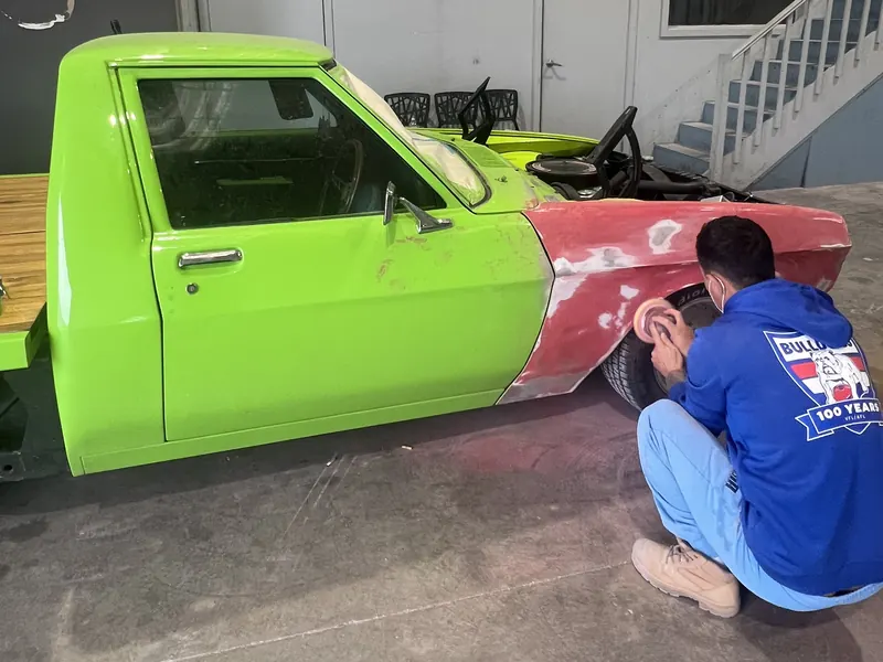 A front guard on a green classic ute being sanded by hand in the workshop