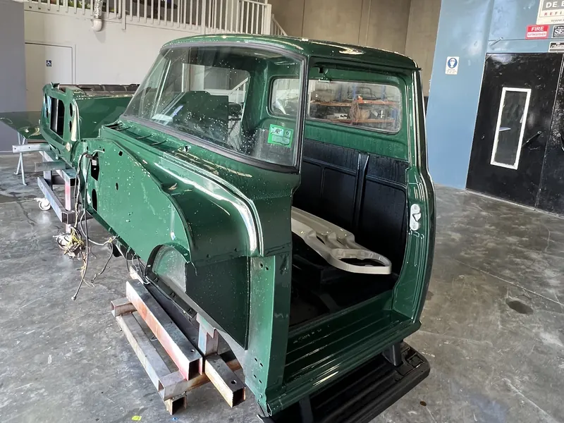 A classic truck cab in fresh green paint beside the spray booth