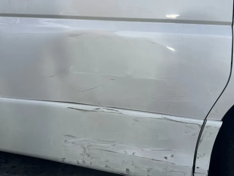 A white van door with a long dent and scrape along the lower half
