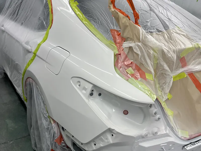 A white sedan masked up in the spray booth with its rear quarter freshly painted