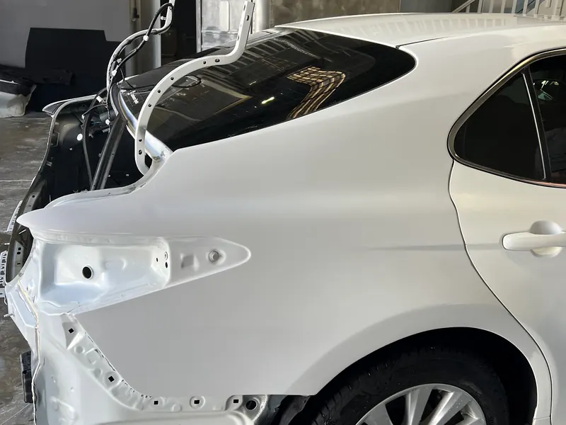 The rear quarter of a white sedan in the workshop with the bumper off